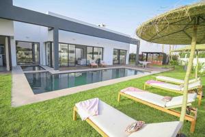 een villa met een zwembad met 2 stoelen en een parasol bij Villa Alanaé avec piscine chauffée in Marrakesh