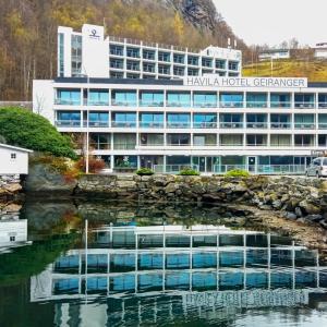 an office building with a reflection in a body of water at Havila Hotel Geiranger in Geiranger
