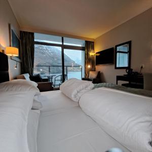 a large white bed in a hotel room with a large window at Havila Hotel Geiranger in Geiranger