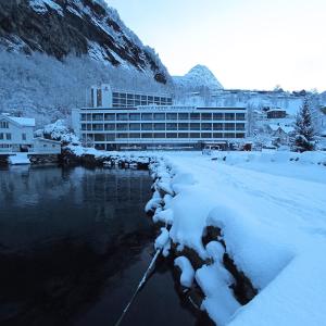 a building with snow on the ground next to a river at Havila Hotel Geiranger in Geiranger