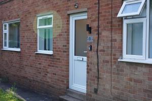 a white door on a brick building with two windows at Cosy 2 bed Apartment 1st Floor Business & Leisure Parking and Wifi by Jesswood Properties in Hinckley