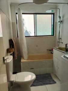 a bathroom with a toilet and a tub and a window at Surfside two-bedroom holiday upstairs in Batemans Bay