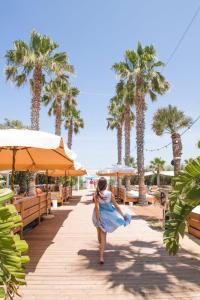 una mujer caminando por una pasarela de madera con palmeras en Masseria Torre Coccaro en Savelletri di Fasano