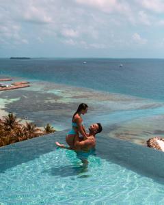 a man and woman sitting in a swimming pool near the ocean at Kaani Palm Beach in Maafushi