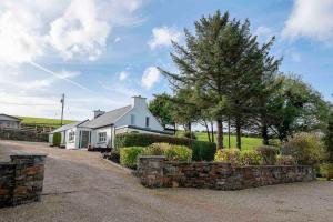 a white house with a stone wall and trees at Traditional Cottage with Private Hot Tub in the Heart of Donegal in Letterkenny