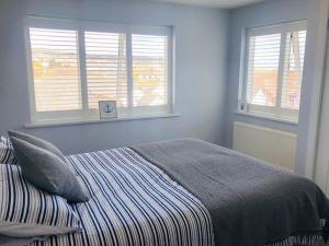 a bedroom with a bed with two windows and a clock at Delightful Dog Friendly Seaside Cottage in Shaldon Devon in Shaldon