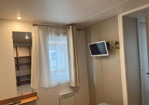 Habitación con ventana y TV en la pared. en Grand mobile-home 45M2 au calme et au bord de mer en Saint-Brevin-les-Pins