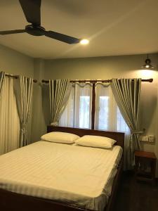 a bedroom with a bed with white sheets and windows at Apsara Khmer House in Siem Reap