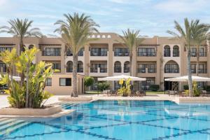 an exterior view of a resort with a pool and palm trees at Jaz Oriental, Almaza Bay in Marsa Matruh