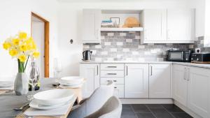 eine Küche mit weißen Schränken und einem Tisch mit gelben Blumen in der Unterkunft Rose Cottage in Buxton