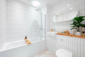 Luxurious two-bedroom flat with scenic views في لندن: حمام من البلاط الأبيض مع حوض استحمام ومغسلة