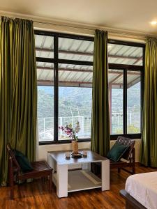a room with a bed and a table and windows at Dhauladhar View Village Resort in Dharmsāla