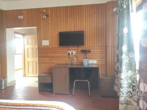 Camera con scrivania e TV su una parete in legno. di Hotel Tayatha a Tawang