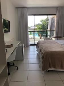 a bedroom with a bed and a desk and a balcony at Iloa Flat Barra São Miguel-Alagoas in Barra de São Miguel