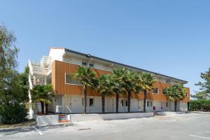 a building with palm trees in front of a parking lot at Sure Hotel by Best Western Rochefort-sur-Mer in Tonnay-Charente