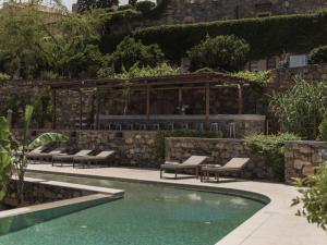 a swimming pool with lounge chairs next to a stone wall at Kinsterna Hotel in Monemvasia