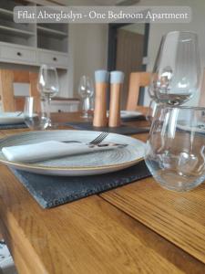 a wooden table with a plate and wine glasses on it at Llew Accommodation - The Townhouse in Beddgelert