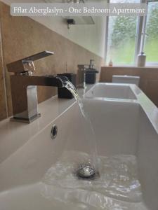 uma torneira de água com água a verter para o lavatório em Llew Accommodation - The Townhouse em Beddgelert
