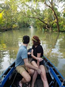 un homme et une femme assis dans un bateau sur l'eau dans l'établissement Can Tho Riverside Hostel, à Bình Thủy