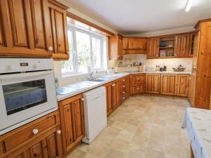 una cocina con armarios de madera y electrodomésticos blancos en Craiglea Cottage, en Coleraine