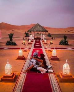 a couple sitting on a red carpet in the desert at Authentic Desert Luxury Camp in Merzouga