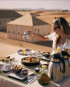 a woman is serving food on a table in the desert at Authentic Desert Luxury Camp in Merzouga