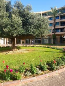 a park with a tree and flowers in front of a building at neot golf kz place in Caesarea