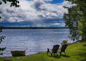 twee stoelen naast een meer met een boot bij Chalet Le Shack O2 in Stratford