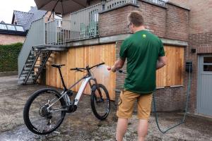 un hombre está lavando una bicicleta delante de una valla en Aan de bosrand, en Opglabbeek