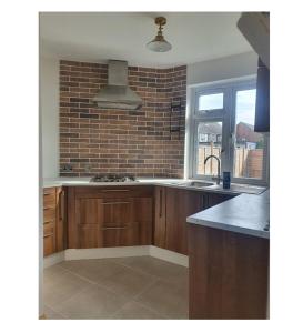 a kitchen with wooden cabinets and a brick wall at Ritzs place in Northolt