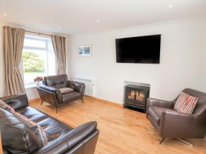 a living room with leather furniture and a flat screen tv at Corncrake Cottage SU in Pollachar