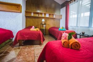 um quarto com três camas com lençóis vermelhos e animais de peluche em Cabañas & Hostal Tojika em Hanga Roa