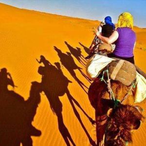 Una mujer montando un camello en el desierto en Travel Oasis Merzouga Camp, en Merzouga