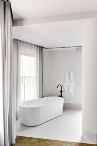a white bathroom with a tub and a window at Central Club Hotel - North Melbourne in Melbourne
