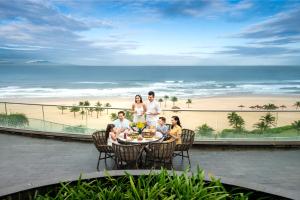 eine Familie, die um einen Tisch auf einer Terrasse mit Strand sitzt in der Unterkunft Vinpearl Resort & Golf Nam Hoi An in Hoi An