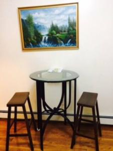 een glazen tafel en twee krukken voor een schilderij bij A private humble abode in Brooklyn