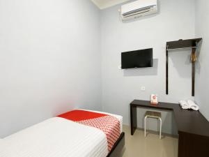 a bedroom with a bed and a desk and a tv at OYO 3160 Guesthouse Pagi Sore Syariah in Padang
