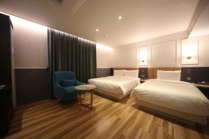 a hotel room with two beds and a blue chair at H Avenue Hotel Minam in Busan