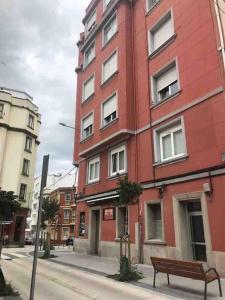 ein rotes Gebäude auf einer Stadtstraße mit einer Bank in der Unterkunft Piso céntrico cerca de la playa in A Coruña