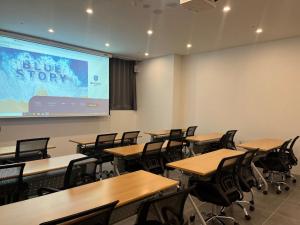 uma sala de aula com mesas e cadeiras e uma tela de projeção em Haeundae Blue Story Hotel em Busan