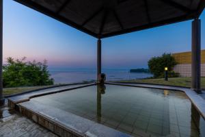 a person sitting next to a swimming pool with a view of the water at Spa and Resort Hotel Solage Oita Hiji Beppuwan in Beppu