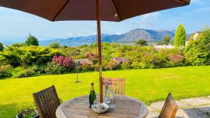 a wooden table with an umbrella and a bottle of wine at Heatherbank Cottage in Onich