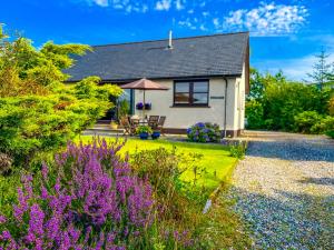 a cottage with a garden with purple flowers at Heatherbank Cottage in Onich