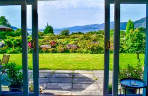 een open deur naar een tuin met uitzicht op het water bij Heatherbank Cottage in Onich