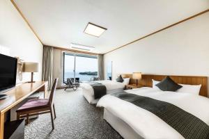 a hotel room with two beds and a desk and a television at Spa and Resort Hotel Solage Oita Hiji Beppuwan in Beppu