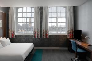 a bedroom with a bed and a desk and two windows at Aloft Liverpool in Liverpool