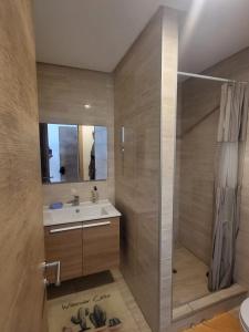 uma casa de banho com um chuveiro, um lavatório e um espelho. em Appartement Plage des Nations Prestigia Front Mer avec grand Jardin em Sidi Bouqnadel