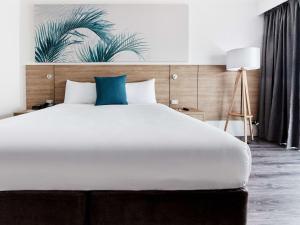 um quarto com uma grande cama branca e uma almofada azul em Novotel Cairns Oasis Resort em Cairns