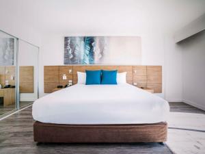 um quarto com uma grande cama branca com almofadas azuis em Novotel Cairns Oasis Resort em Cairns