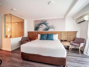 Novotel Cairns Oasis Resort في كيرنز: غرفة نوم بسرير كبير وكرسيين